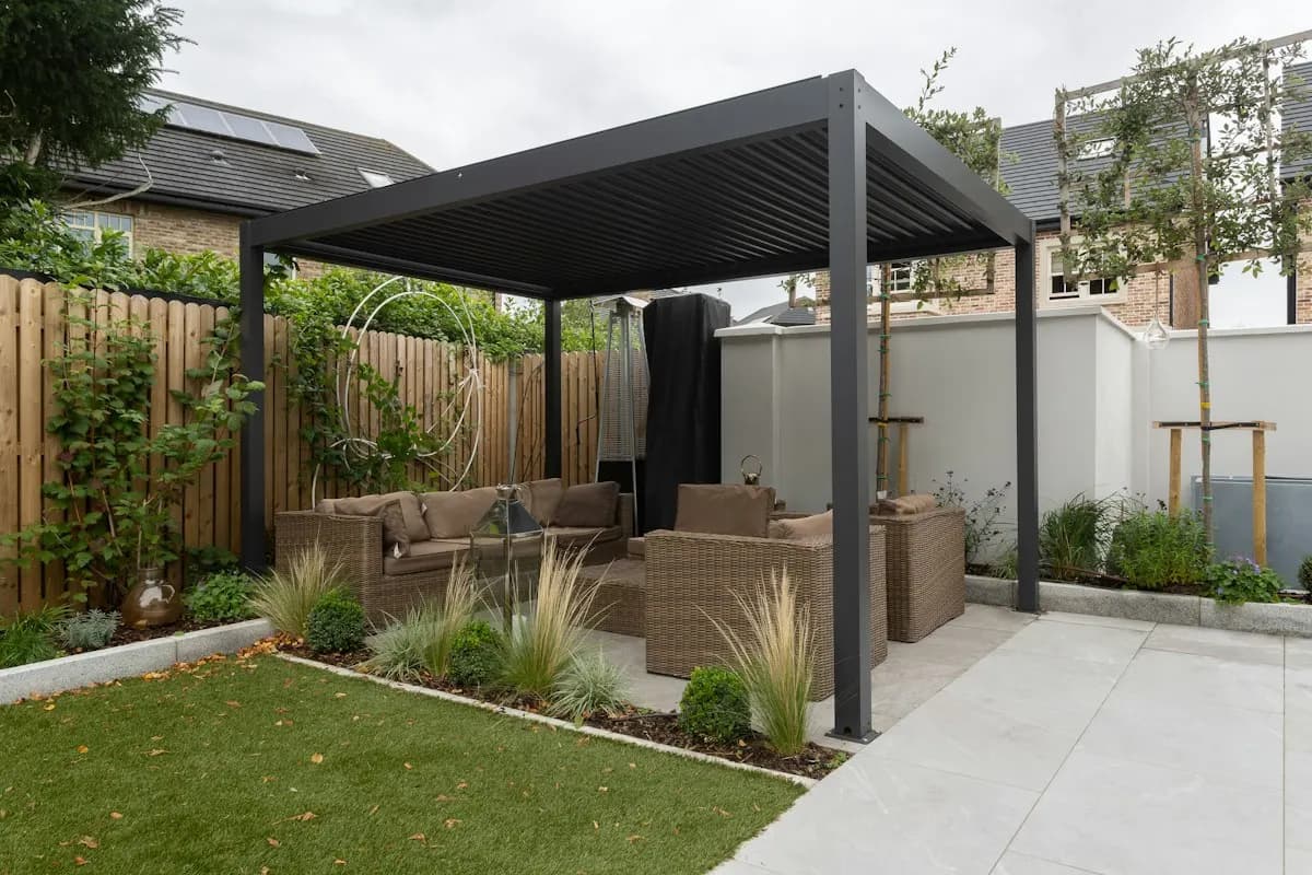 Freestanding dark pergola beside a paved garden terrace